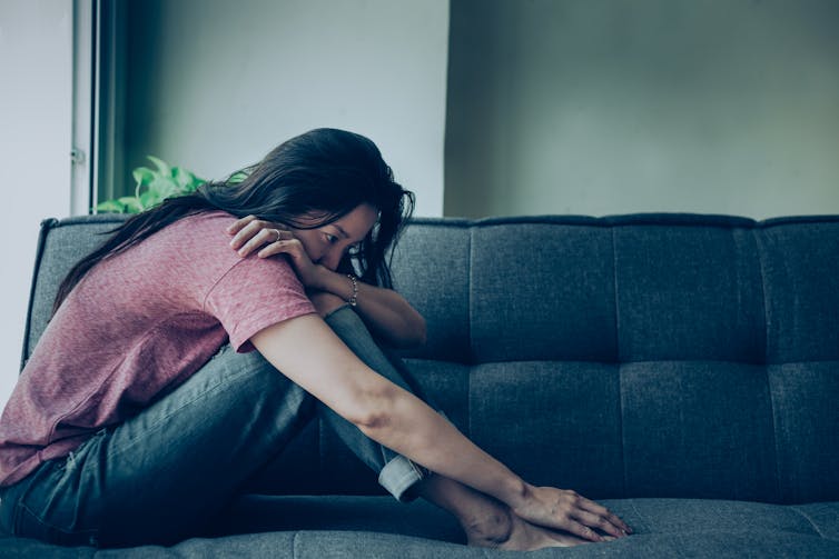 A woman hunched over on the couch at home, appearing lonely or depressed.