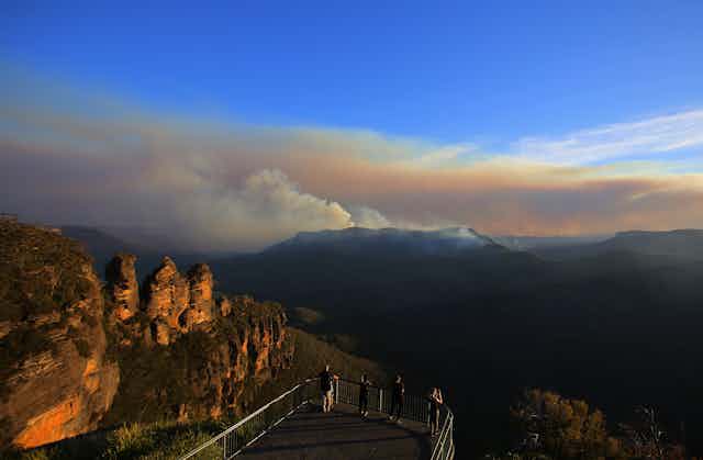 The Three Sisters rock formation is seen as people watch smoke int he distance from the Black Summer fires