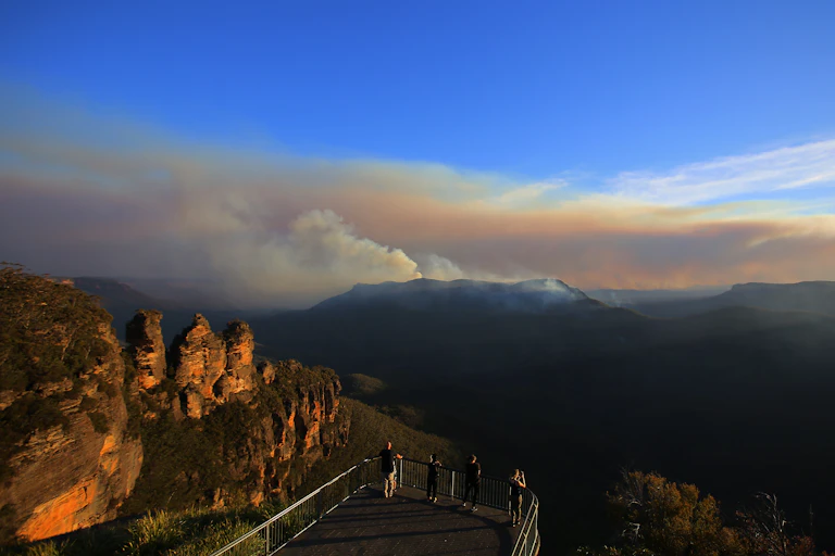 The Three Sisters rock formation is seen as people watch smoke int he distance from the Black Summer fires