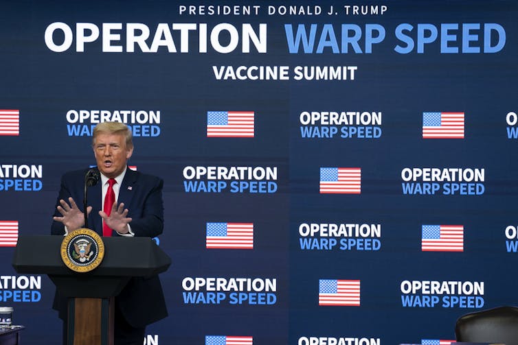 President Donald Trump stands at a podium in front of an Operation Warp Speed banner