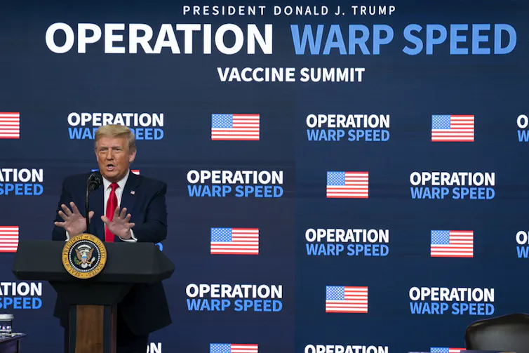 President Donald Trump stands at a podium in front of an Operation Warp Speed banner
