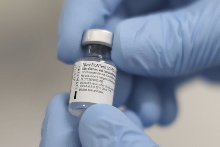 Gloved hands holding a vial of vaccine