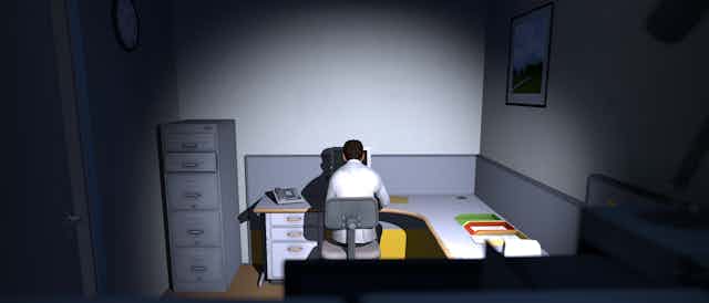 Man sitting in an office cubicle, looking at a computer.