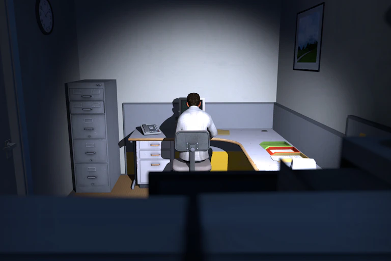 Man sitting in an office cubicle, looking at a computer.