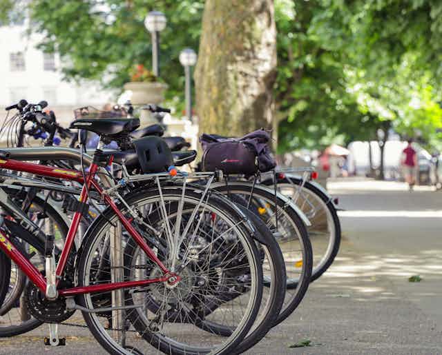 A row of parked bikes on a tree-lined British street.