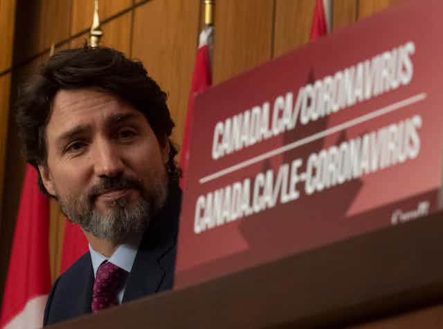 Justin Trudeau sits next to a coronavirus placard