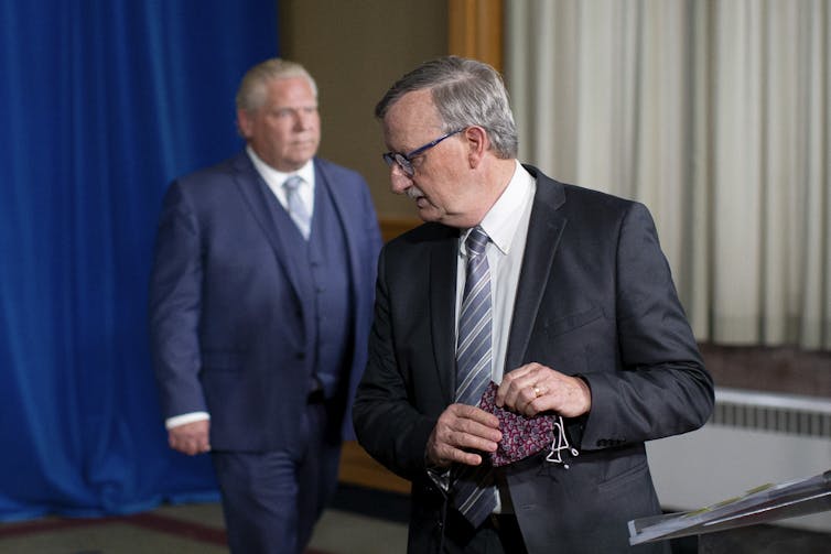 David Williams walks away from a microphone as Doug Ford approaches