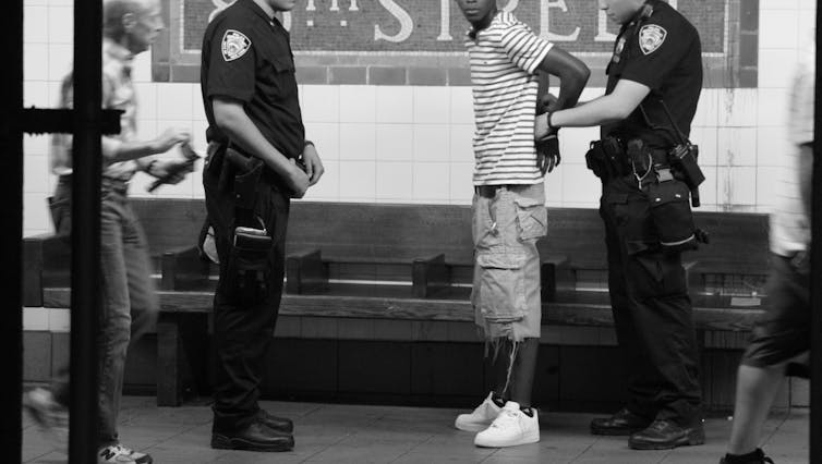 Black and whit image of police arresting a Black man in a New York subway station; no faces are seen