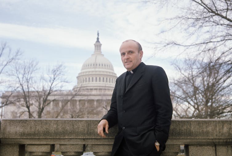 Rep. Robert Drinan, wearing his clerical collar, poses in front of the U.S. Capitol.