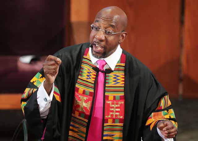 Raphael Warnock, wearing a stole, gestures during a sermon.