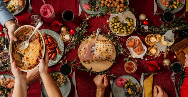 Someone passes a dish filled with food to someone else amid a table that displays many types of holiday foods.