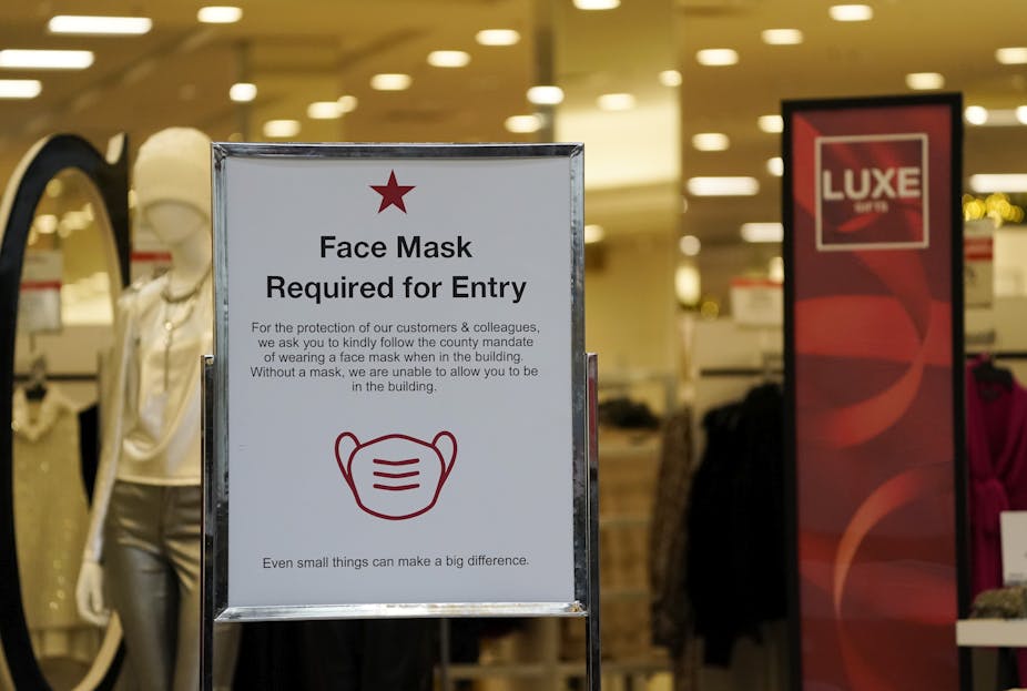 A sign advises holiday shoppers of the need for masks to enter a Macy's department store at a mall in Lone Tree, Colo. 