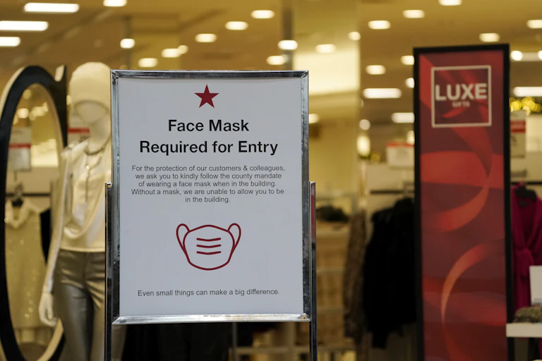 A sign advises holiday shoppers of the need for masks to enter a Macy's department store at a mall in Lone Tree, Colo.