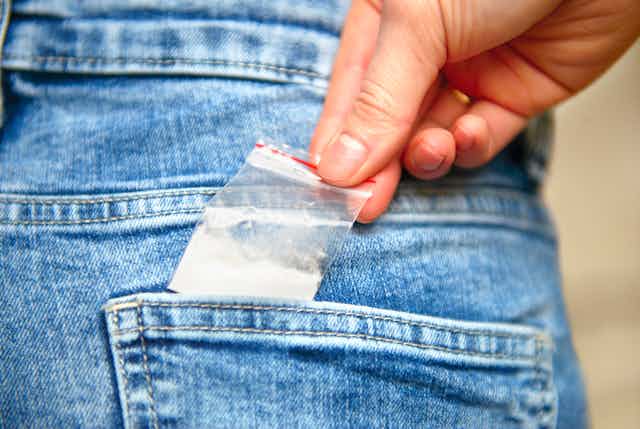 Small bag of white powder is pulled out of a jeans pocket
