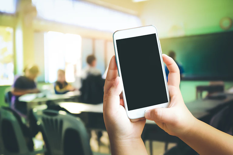 Student holding up mobile phone with classroom in the background.