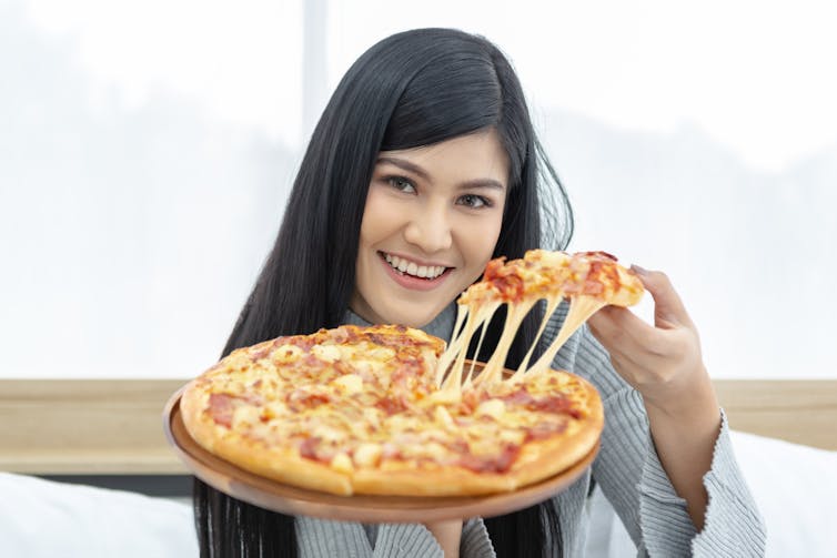 A woman in bed holding a pizza.