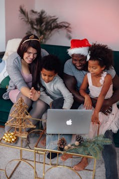 A family wearing holiday hats gathered around a laptop near Christmas decorations