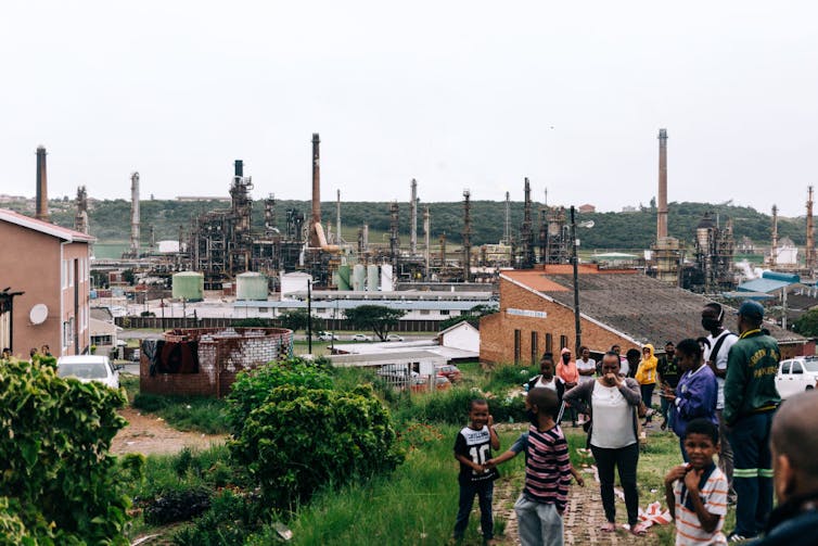 A crowd of people, including children, gathered near an oil refinery, which is located in a residential area.