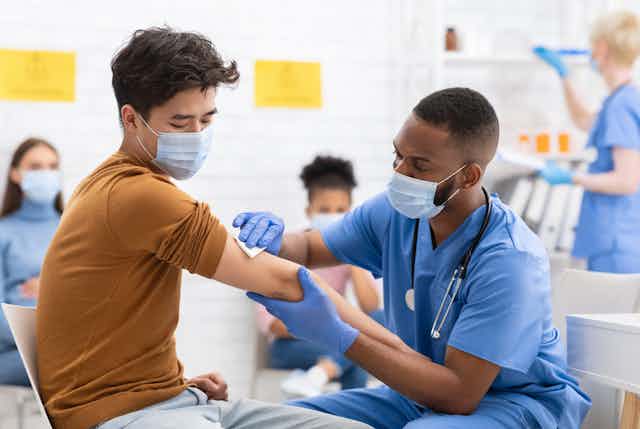 A nurse in a mask vaccinating a man in a mask