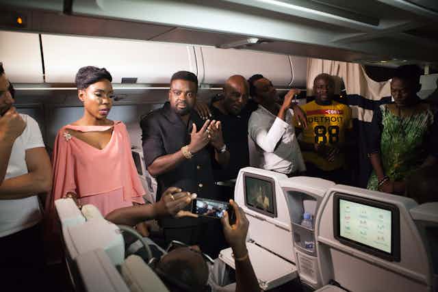 A group of actors seated on a plane having a conversation.