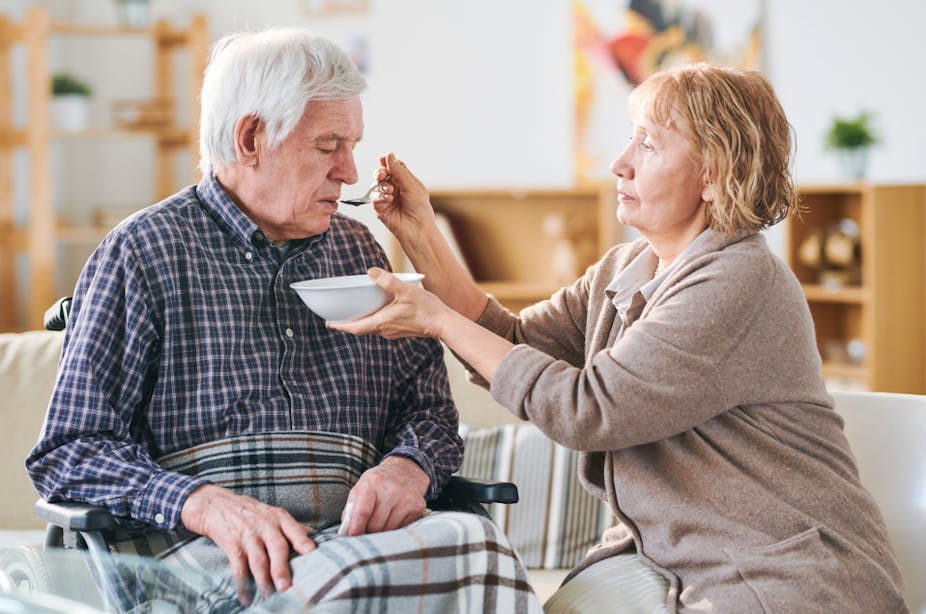 A woman feeding an elderly man who has had a stroke.