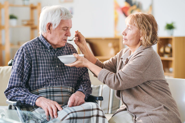 A woman feeding an elderly man who has had a stroke.