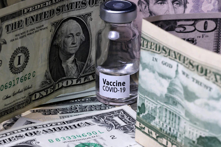 A vial of COVID-19 vaccine amidst a stack of cash.