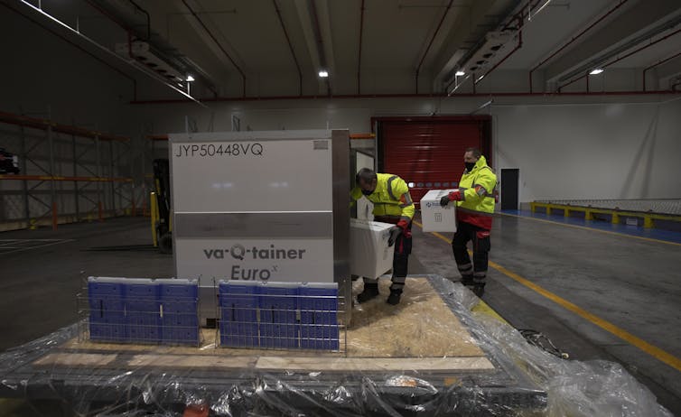 Workers handling a shipment of vaccines in a large cold storage container.