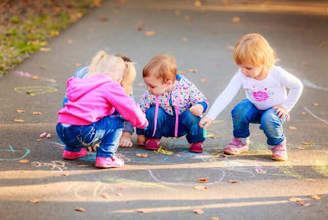 young children drawing with chalk on footpath