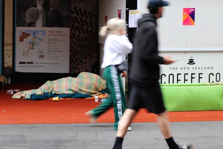 Pedestrians walking past homeless person in street