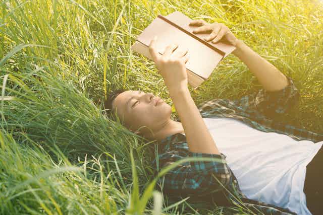 Young adult boy lying on the grass reading.
