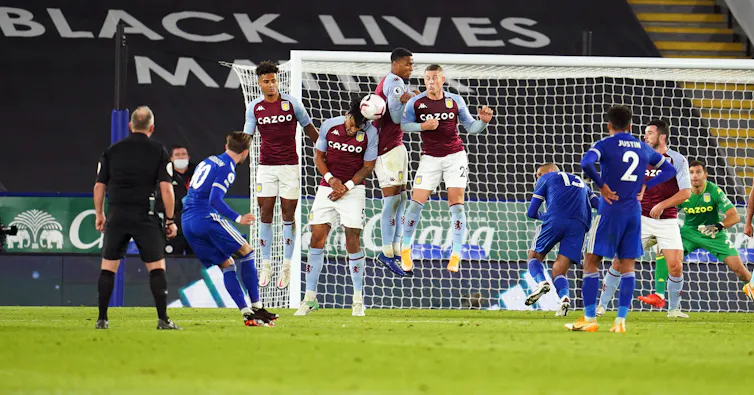 `Footballers defending a goal from a free kick.
