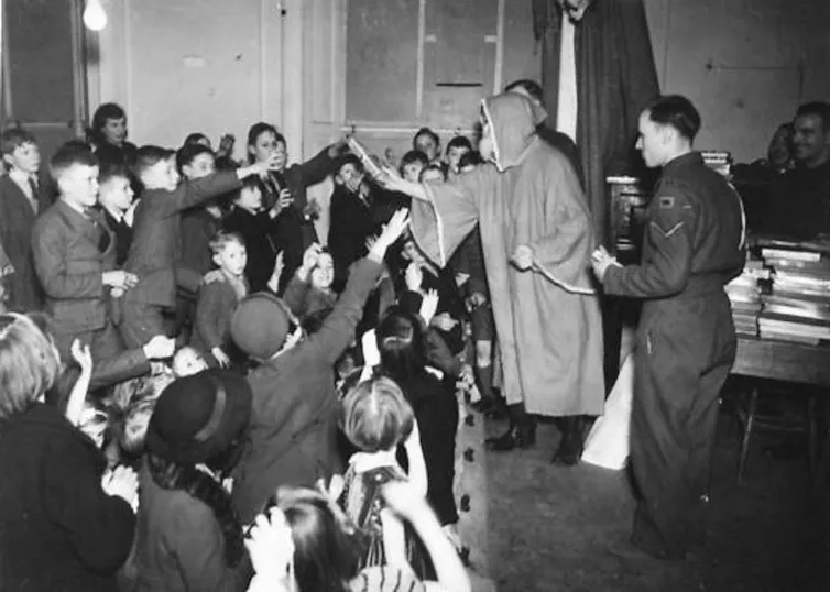 1940 photo of a soldier dressed as Santa Claus giving presents to a group of children.