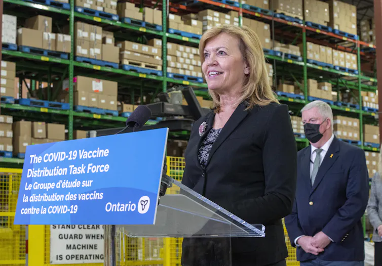 Christine Elliott stands at a podium with sign reading THE COVID-19 DISTRIBUTION TASK FORCE