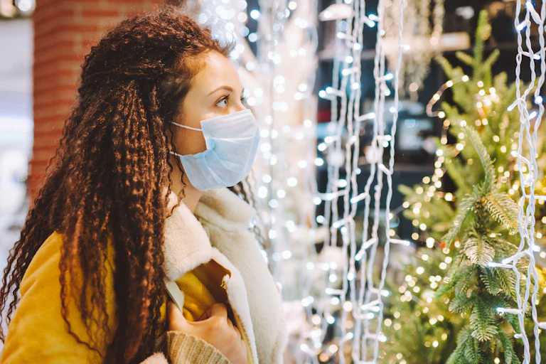 A woman in a face mask looking at a Christmas tree and Christmas lights