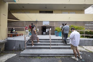 Línea de personas con mascarillas en el exterior de un edificio