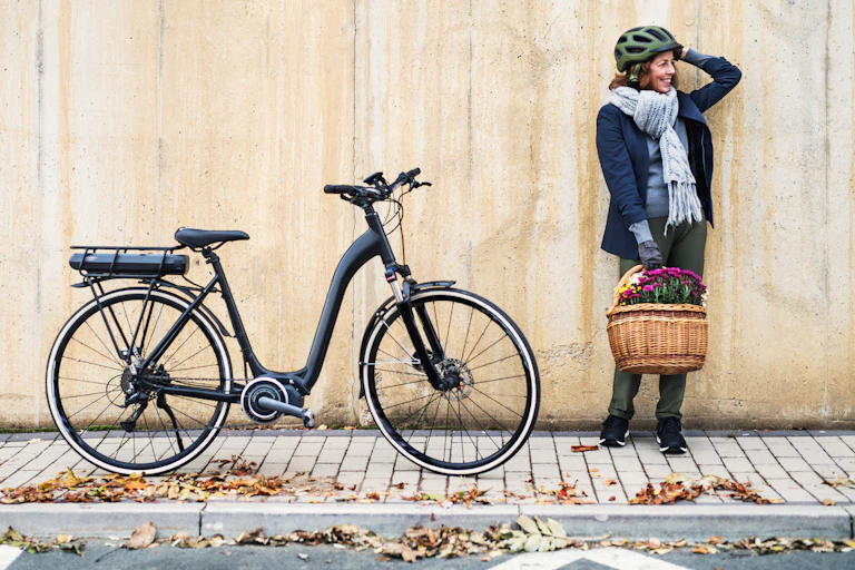 A woman holding a basket stands next to and electric bicycle.