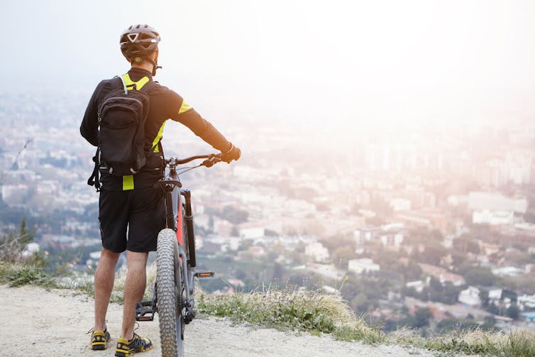 A man with a bike looks out on a city below him.