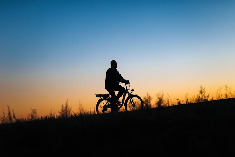 A silhouette of a person riding a e-bike against a sunset background.