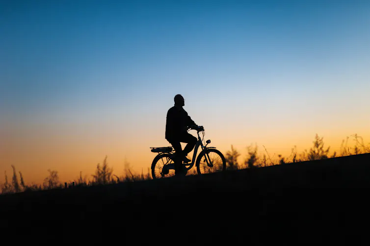 A silhouette of a person riding a e-bike against a sunset background.