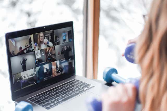 A woman teaching an online fitness class in front of a laptop