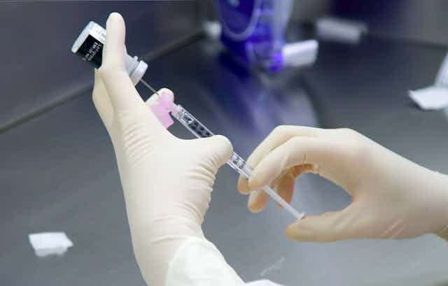 Glove hands preparing the Pfizer vaccine against COVID.