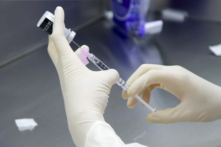 Glove hands preparing the Pfizer vaccine against COVID.