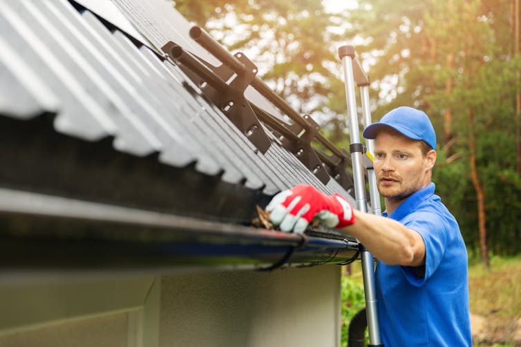 A man cleans leaf litter out of gutters.