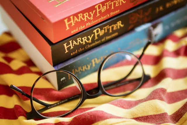 A pile of three Harry Potter books with a pair of reading glasses on a red and yellow striped cloth