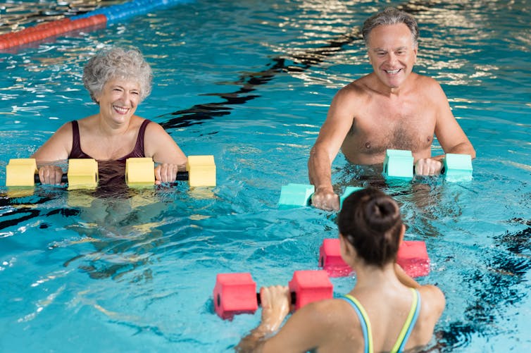 Older couple smile while performing water aerobics with a trainer.