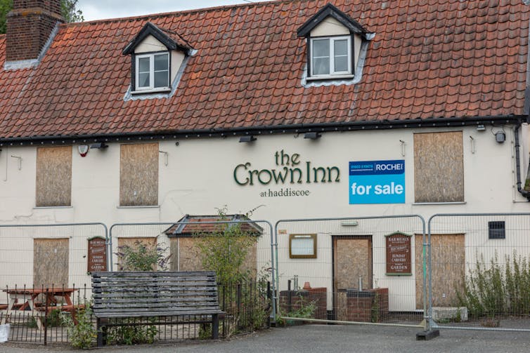 Pub with boarded up windows and for sale sign.