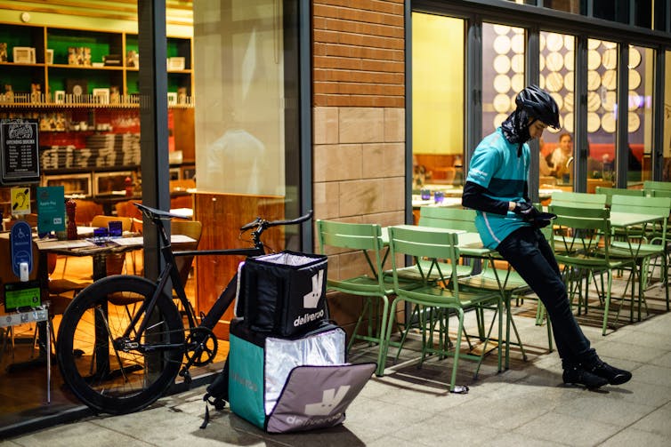A Deliveroo delivery cyclist waits outside of a restaurant