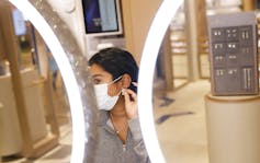 A woman in a mask looks in a mirror as she tried on earrings.