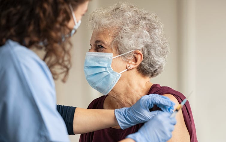 An elderly woman in a mask being vaccinated